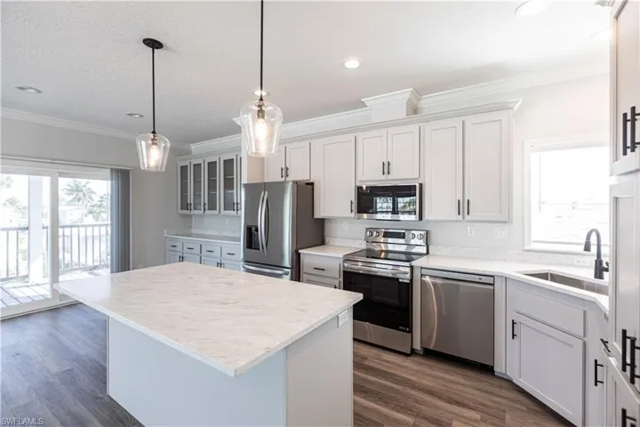 Kitchen with appliances with stainless steel finishes, a center island, white cabinets, ornamental molding, and pendant lighting