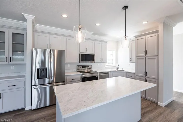 Kitchen featuring ornamental molding, stainless steel appliances, decorative light fixtures, dark wood-style flooring, and a center island
