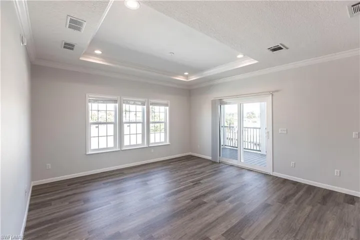 Unfurnished room with crown molding, dark wood finished floors, healthy amount of natural light, a tray ceiling, and recessed lighting