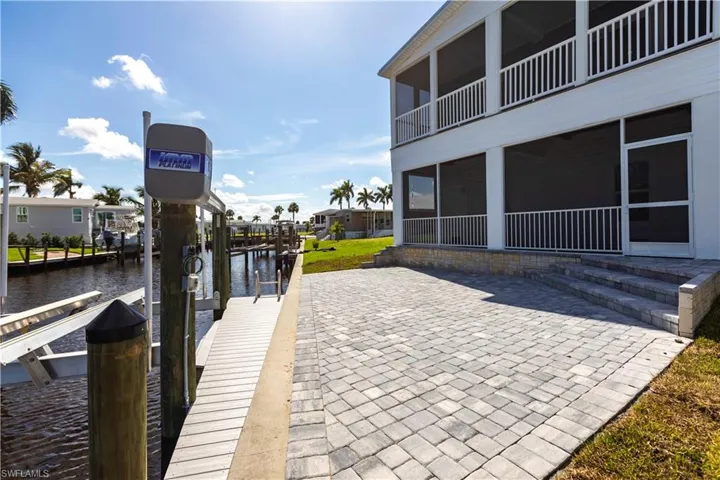 Dock area with a sunroom, boat lift, a water view, and a patio area
