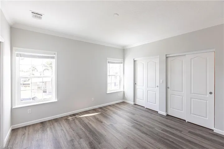 Unfurnished bedroom with multiple closets, crown molding, and wood finished floors
