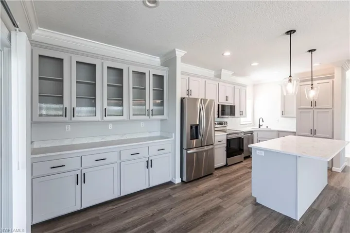 Kitchen featuring appliances with stainless steel finishes, glass insert cabinets, crown molding, pendant lighting, and a center island