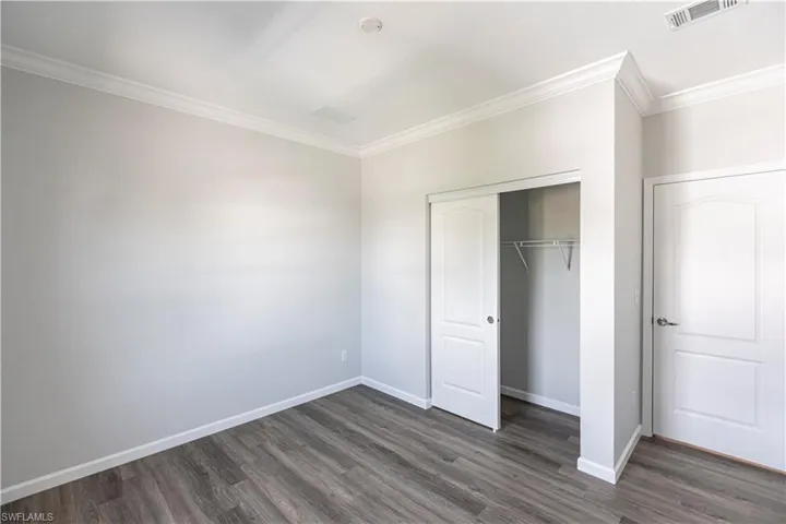 Unfurnished bedroom featuring ornamental molding, dark wood-style floors, and a closet