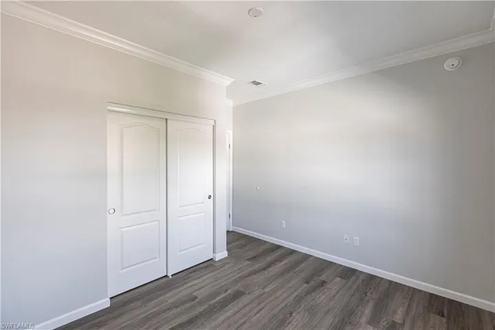 Unfurnished bedroom featuring dark wood-type flooring, a closet, and crown molding