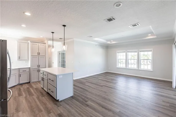 Kitchen featuring crown molding, freestanding refrigerator, a center island, a tray ceiling, and pendant lighting
