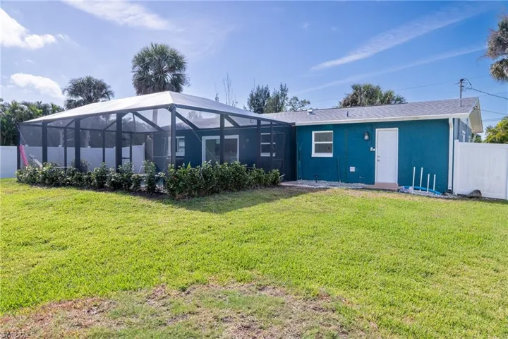 Back of house featuring a lanai, fence, stucco siding, and a yard