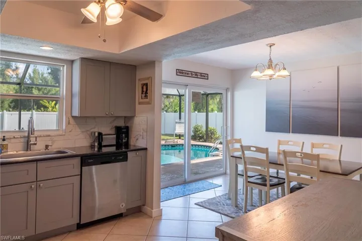 Kitchen featuring light tile patterned floors, gray cabinetry, stainless steel dishwasher, backsplash, and a sink