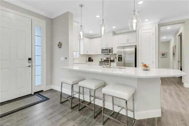 Kitchen with wood finish floors, a breakfast bar area, a peninsula, white cabinetry, and ornamental molding