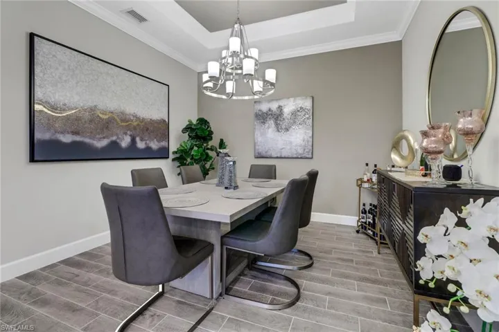 Dining space featuring wood finish floors, a raised ceiling, crown molding, and suspended lighting