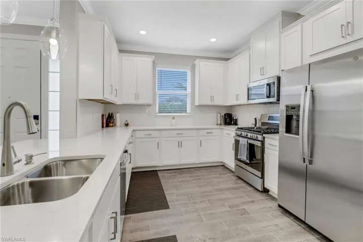 Kitchen with stainless steel appliances, white cabinets, ornamental molding, pendant lighting, and light stone counters