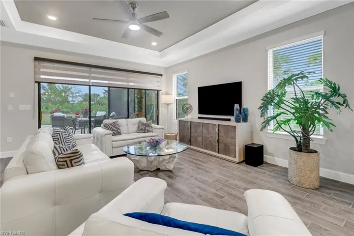 Living area featuring wood finish floors, a ceiling fan, a tray ceiling, crown molding, and recessed lighting