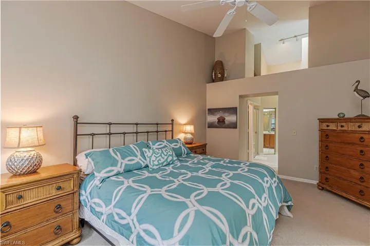 Carpeted bedroom with ceiling fan, ensuite bathroom, and high vaulted ceiling
