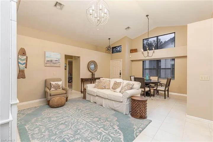Living room featuring light tile patterned floors, vaulted ceiling, and an inviting chandelier