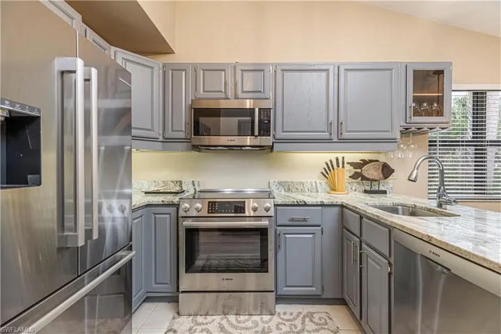 Kitchen with gray cabinets, light tile patterned floors, sink, and appliances with stainless steel finishes