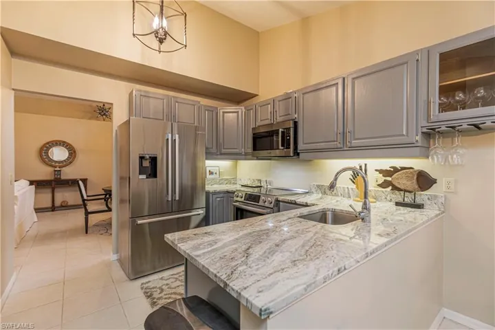 Kitchen with light stone countertops, kitchen peninsula, stainless steel appliances, sink, and hanging light fixtures