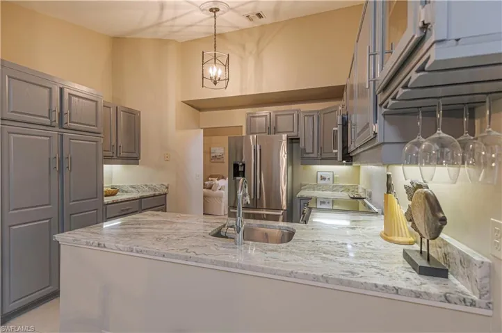 Kitchen featuring hanging light fixtures, sink, appliances with stainless steel finishes, light stone counters, and kitchen peninsula