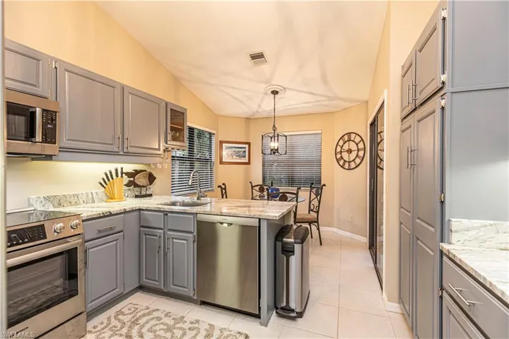 Kitchen featuring kitchen peninsula, appliances with stainless steel finishes, decorative light fixtures, gray cabinets, and lofted ceiling