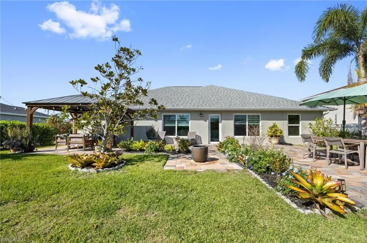 Rear view of house featuring a patio area, a yard, stucco siding, and a shingled roof