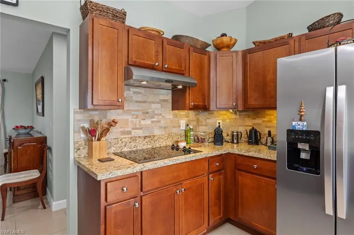 Kitchen featuring stainless steel fridge, under cabinet range hood, brown cabinetry, and backsplash