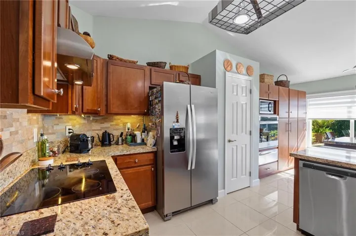 Kitchen featuring stainless steel appliances, light tile patterned floors, extractor fan, light stone countertops, and lofted ceiling