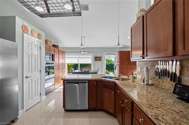 Kitchen with a peninsula, stainless steel appliances, light stone countertops, hanging light fixtures, and tasteful backsplash