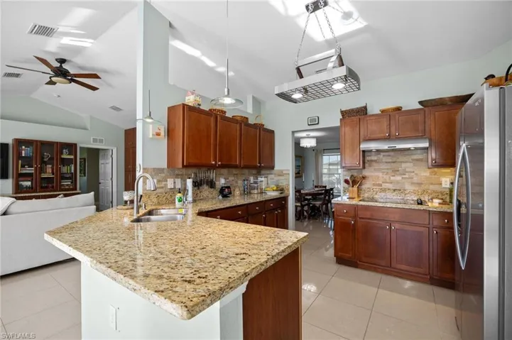 Kitchen with freestanding refrigerator, a peninsula, light tile patterned floors, lofted ceiling, and light stone counters
