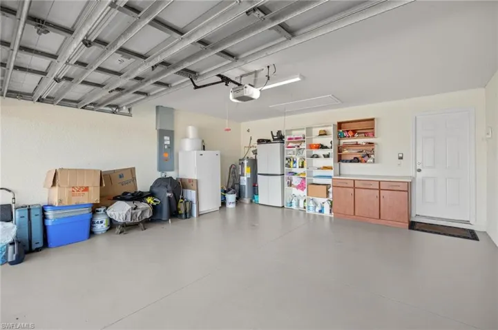 Garage featuring freestanding refrigerator, electric panel, electric water heater, and a garage door opener