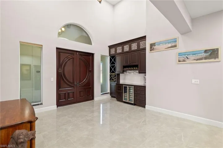 Entrance foyer with a bar, beverage cooler, marble finish floor, a towering ceiling, and baseboards