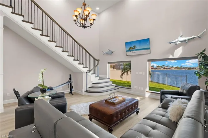 Living room featuring baseboards, a towering ceiling, a notable chandelier, wood finished floors, and stairs