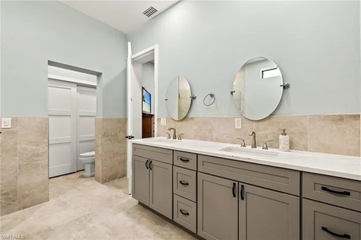 Full bath featuring a wainscoted wall, a sink, visible vents, and tile walls