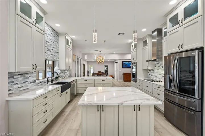 Kitchen with wall chimney exhaust hood, a peninsula, a sink, visible vents, and appliances with stainless steel finishes