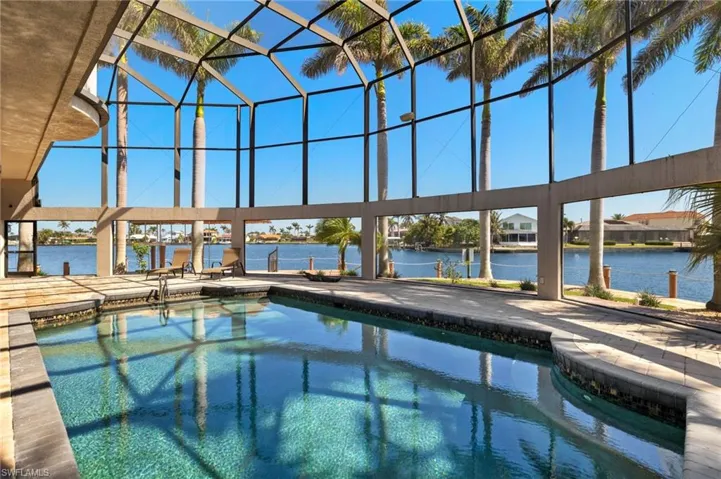 Pool featuring glass enclosure, a patio area, and a water view