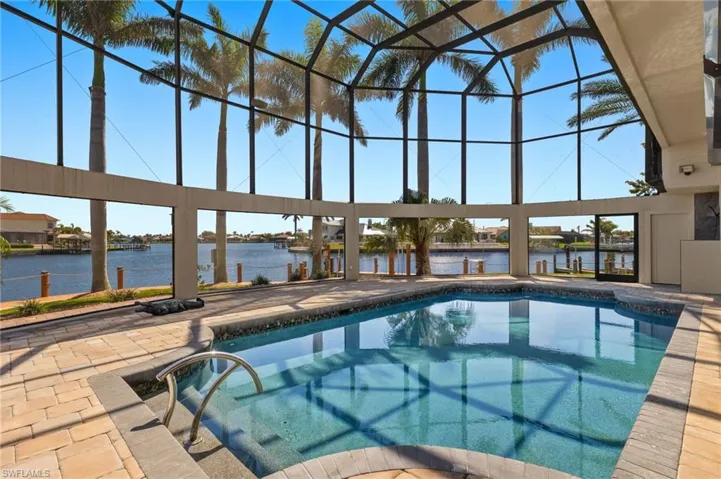 Outdoor pool with glass enclosure, a patio area, and a water view