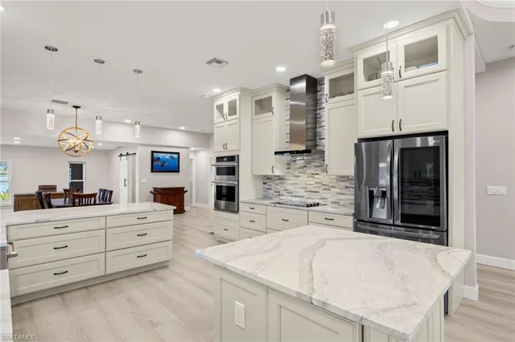 Kitchen with light wood finished floors, stainless steel appliances, decorative light fixtures, wall chimney exhaust hood, and decorative backsplash