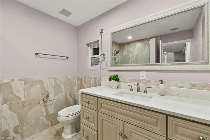 Spare Bathroom with visible vents, toilet, vanity, tile walls, and a shower