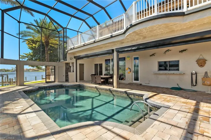 Outdoor pool with glass enclosure, a water view, and a patio