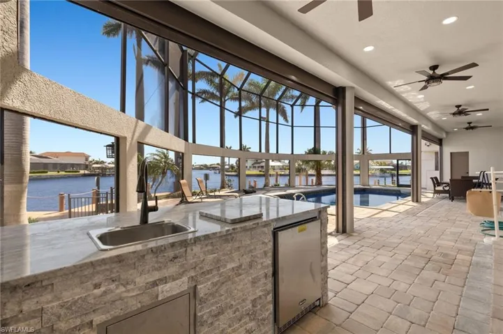 View of patio / terrace with an outdoor kitchen, a ceiling fan, a sink, an outdoor pool, and a water view