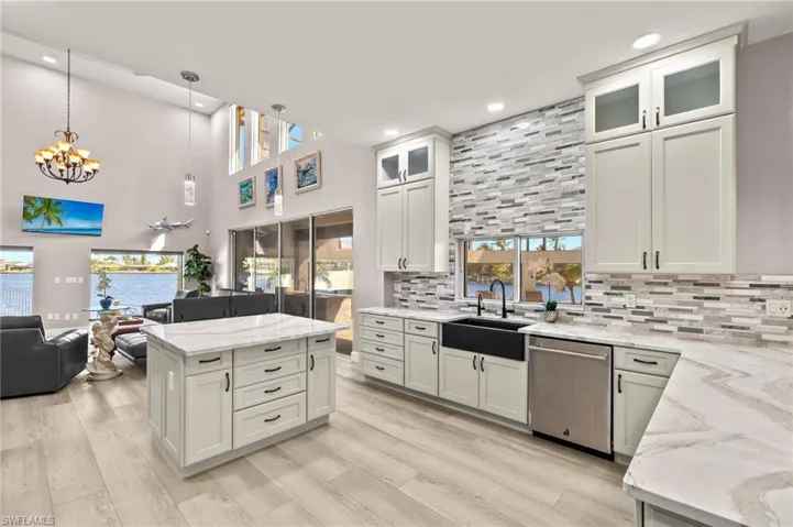Kitchen with light stone counters, stainless steel dishwasher, a sink, open floor plan, and a notable chandelier