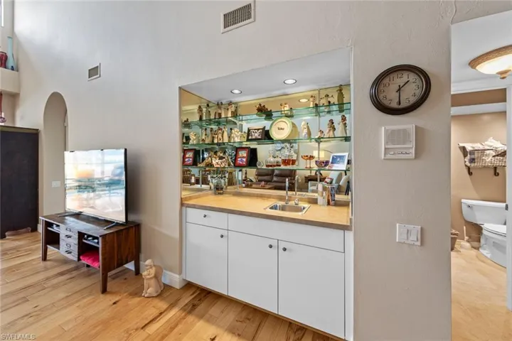 Bar with light wood-type flooring, white cabinets, and sink