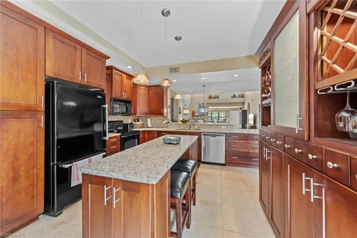 Kitchen with a kitchen breakfast bar, light stone countertops, black appliances, a center island, and hanging light fixtures
