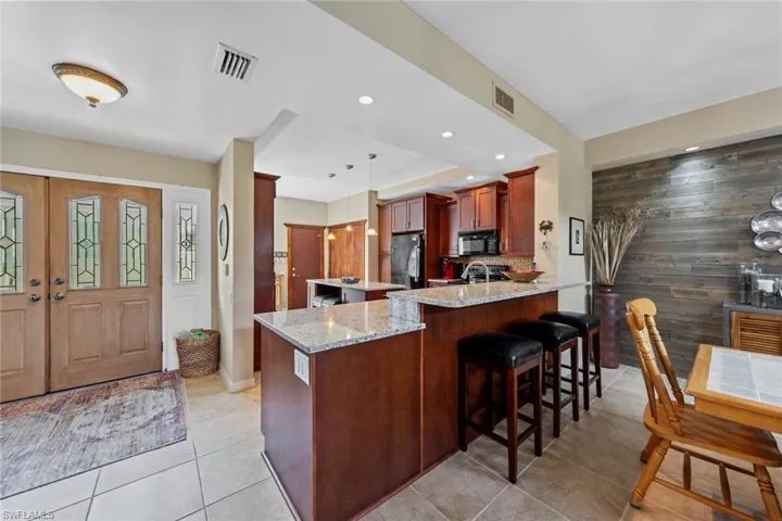 Kitchen with hanging light fixtures, light stone counters, stainless steel refrigerator, kitchen peninsula, and a breakfast bar area