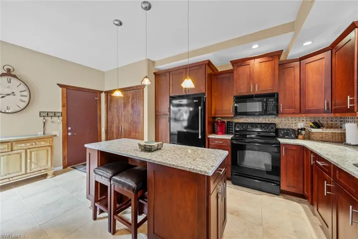 Kitchen featuring a kitchen island, light stone countertops, black appliances, tasteful backsplash, and hanging light fixtures