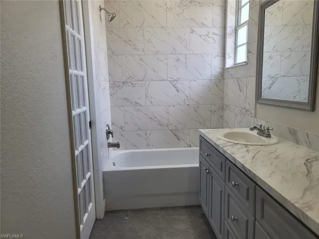 Bathroom with shower / bathtub combination, vanity, and a textured wall