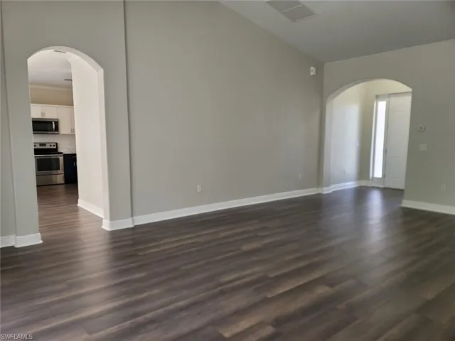 Unfurnished living room featuring arched walkways, dark wood-style flooring, and vaulted ceiling
