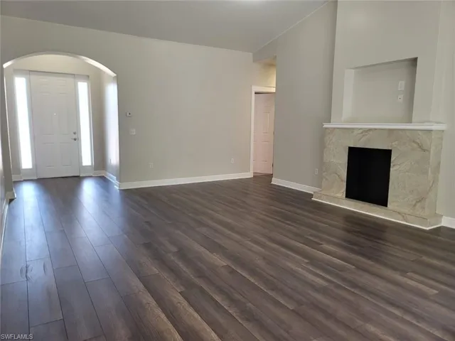 Unfurnished living room featuring arched walkways, dark wood-style floors, vaulted ceiling, and a premium fireplace