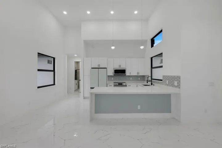Kitchen featuring freestanding refrigerator, stainless steel range with electric cooktop, light countertops, light marble finish flooring, and a towering ceiling