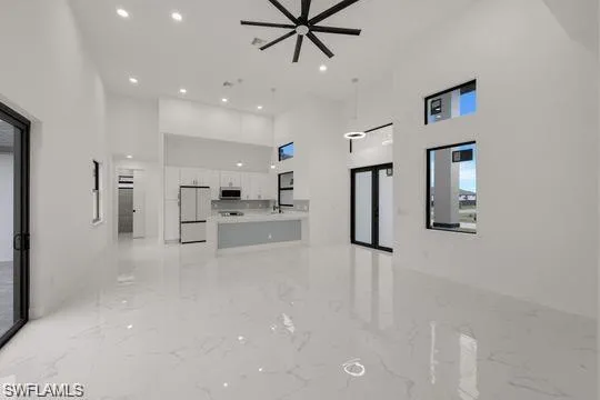 Unfurnished living room featuring a towering ceiling, light marble finish flooring, recessed lighting, and a ceiling fan