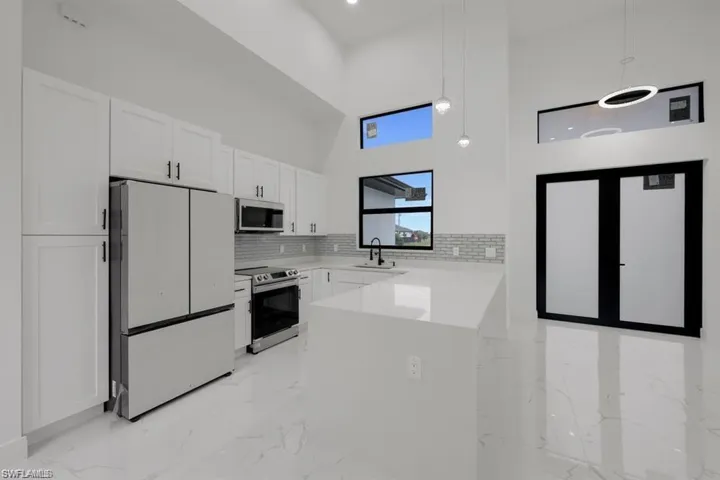 Kitchen with stainless steel appliances, a high ceiling, light marble finish flooring, white cabinets, and tasteful backsplash