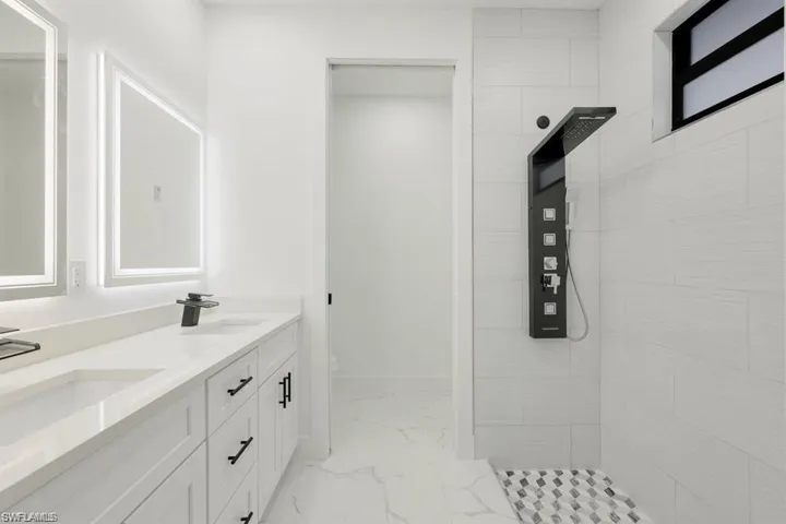 Bathroom featuring marble finish floors, double vanity, and tiled shower
