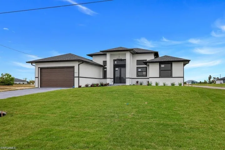 Prairie-style home featuring stucco siding, a garage, a front yard, and driveway